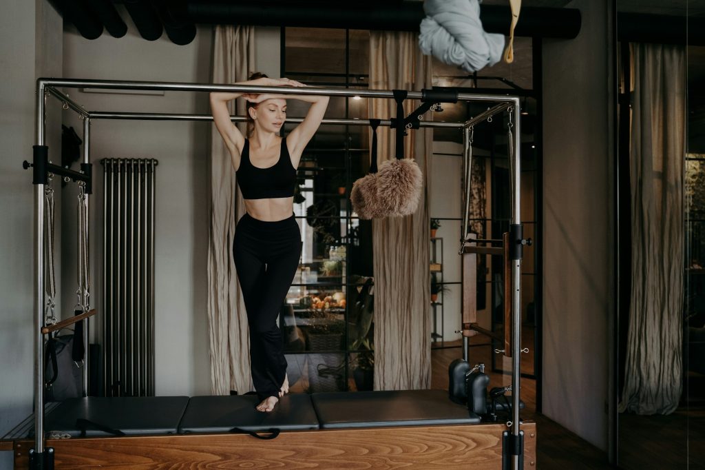 Young slim caucasian female resting on bar of pilates cadillac reformer